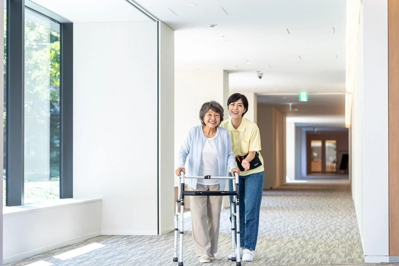 歩行器を使用する高齢女性を若い女性がサポートしながら歩いている様子