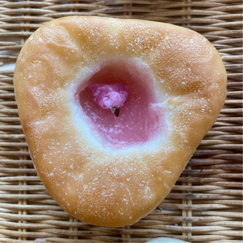 カゴの上に置かれた、中央にピンク色のフィリングと桜の花が飾られた菓子パン。春の訪れを感じさせる、可愛らしくて美味しそうな一品です。