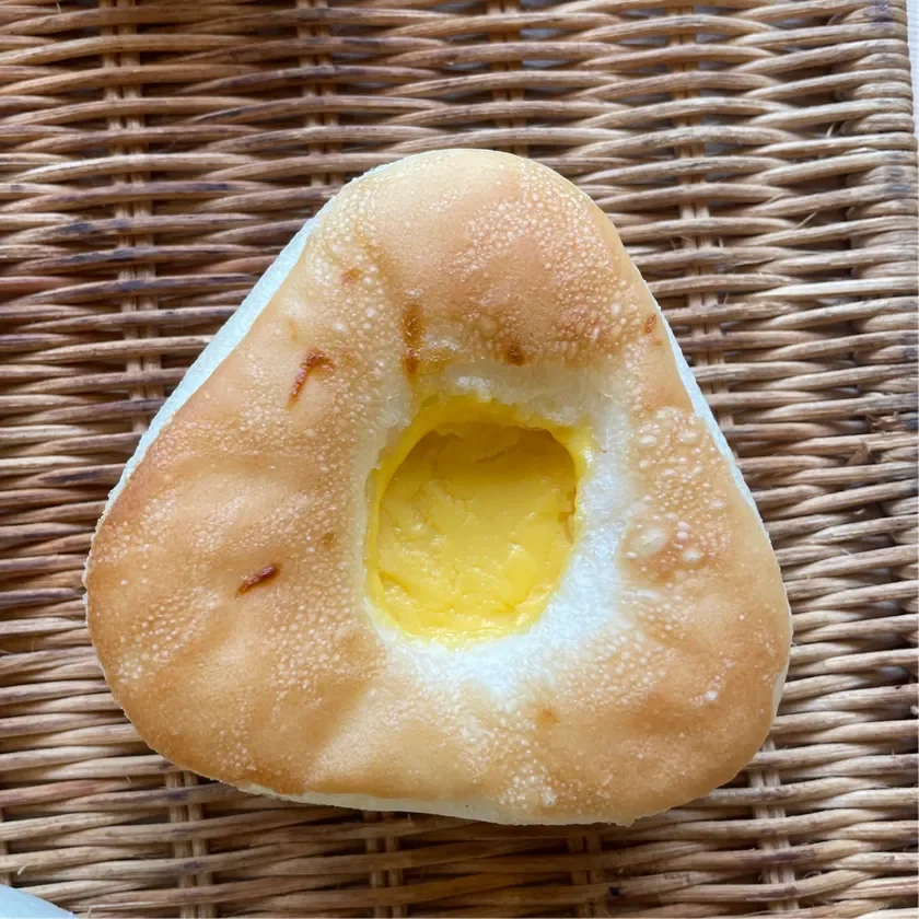 籠の上に置かれた、三角形の形状をしたカスタードクリーム入りのパンです。表面はこんがりと焼き色がついています。