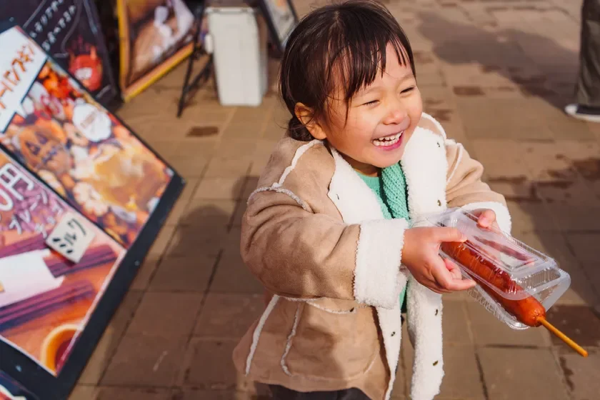 屋外イベントでコーン犬を楽しむ子供の笑顔