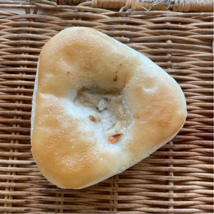 編みかごの上に置かれた、三角形の形をした菓子パンのクローズアップ画像です。表面は薄い茶色で、中央部分にはわずかな凹みが見られ、素朴な雰囲気が漂っています。