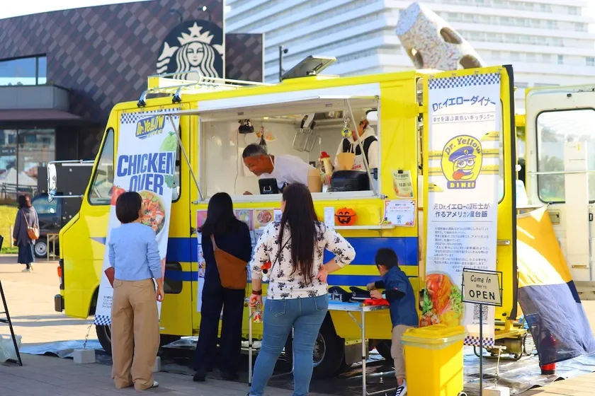 黄色いキッチンカー「Dr.イエローダイナー」がアメリカン屋台飯を提供している様子